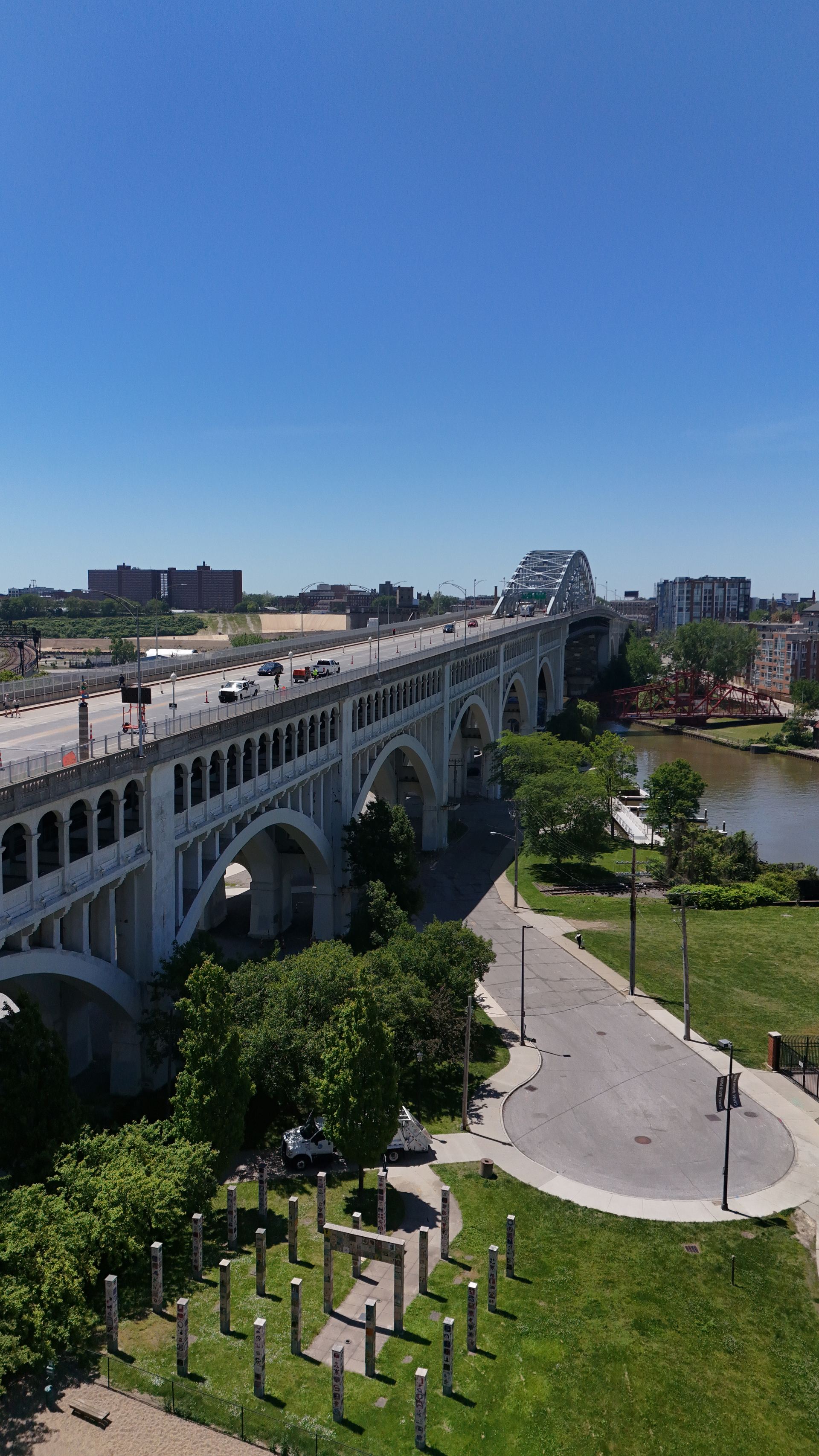 Vertical aerial photograph looking down the arched spans of the Detroit–Superior Bridge toward the Cuyahoga River and a red lift bridge — Stratum Aerial Media