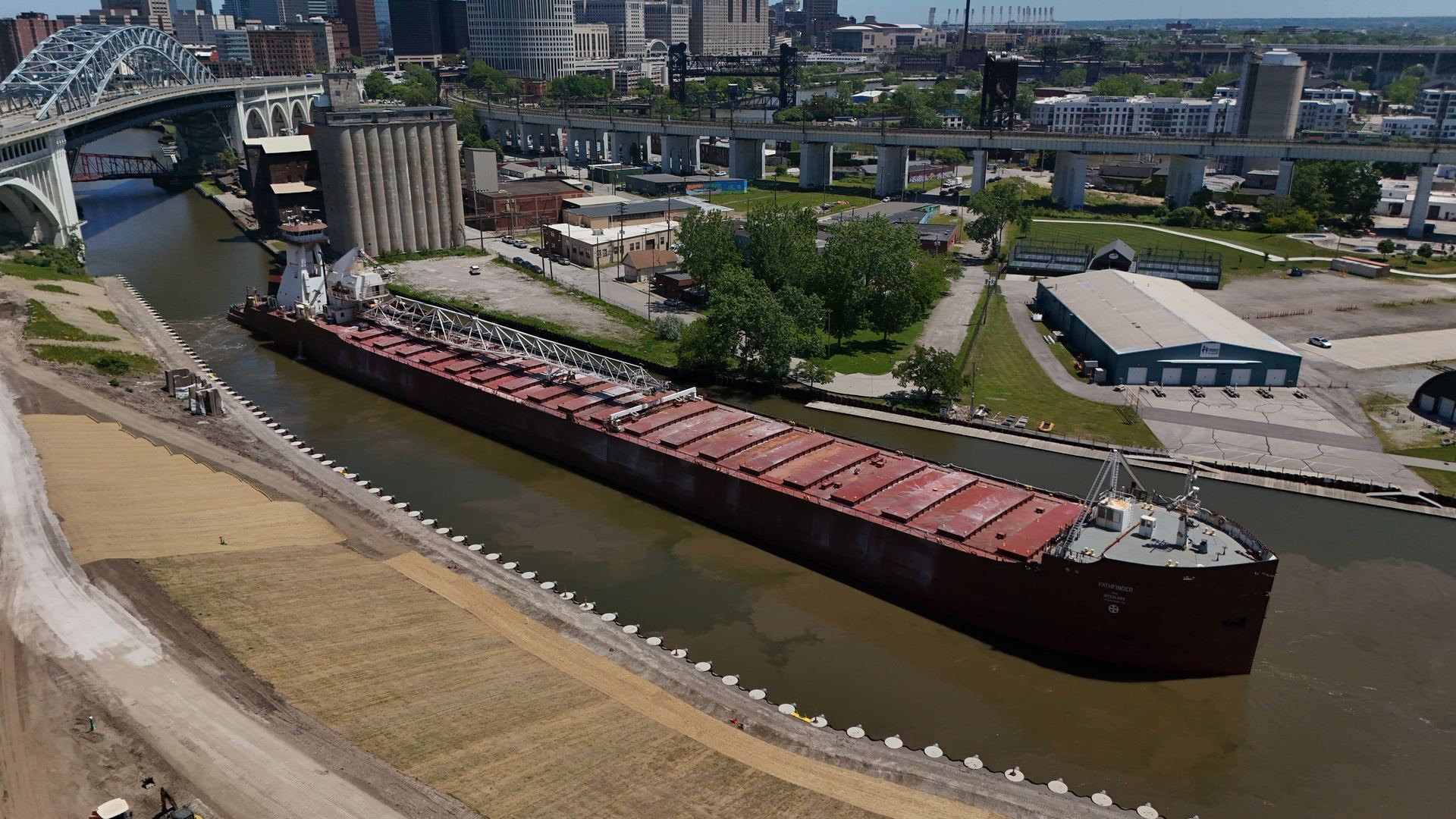 Aerial view of a Great Lakes freighter fully docked on the Cuyahoga River with the Cleveland skyline behind — Stratum Aerial Media